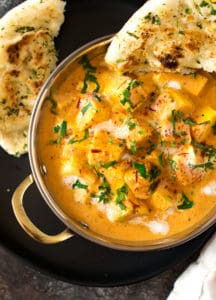 Shahi paneer on a black plate served with warm naan.